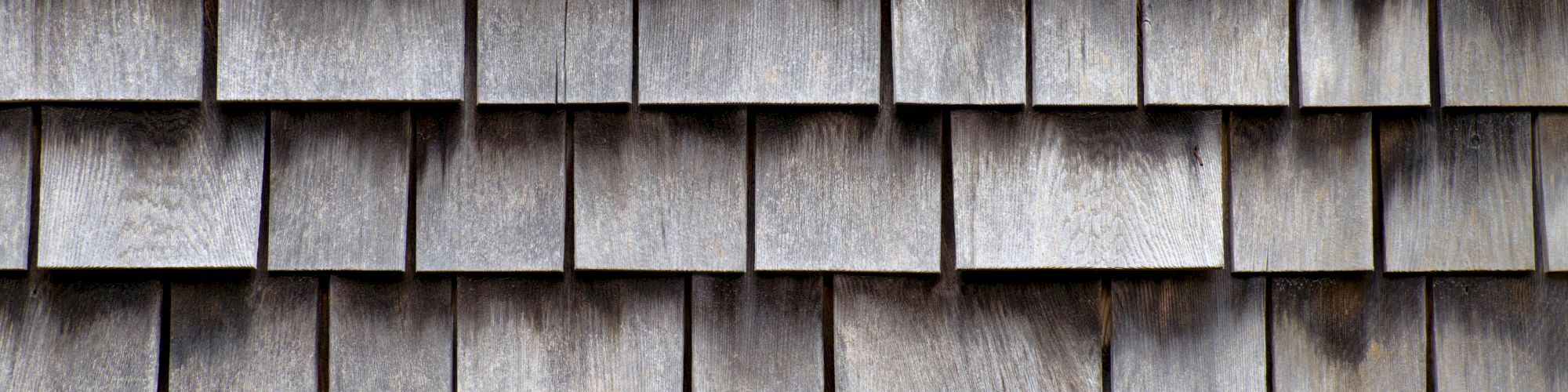 The image shows a close-up of a wall with wooden shingles, arranged in overlapping rows to create a textured surface.